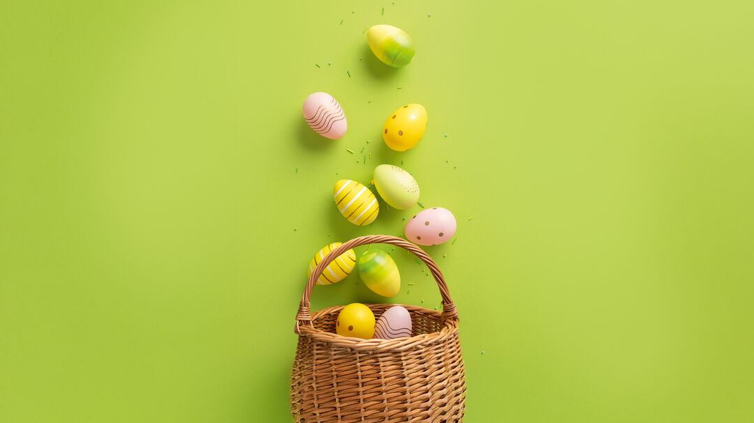 Korb mit bunten Ostereiern auf grünem Hintergrund